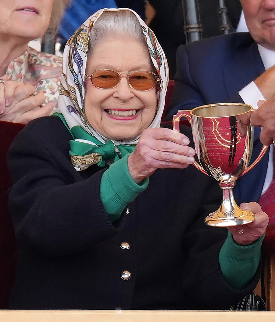 Королеве Елизавете II вручают кубок за победу её лошади на скачках во время второго дня Королевского Виндзорского конного шоу в Хоум-парке, 13 мая 2022 года в Виндзоре, Англия